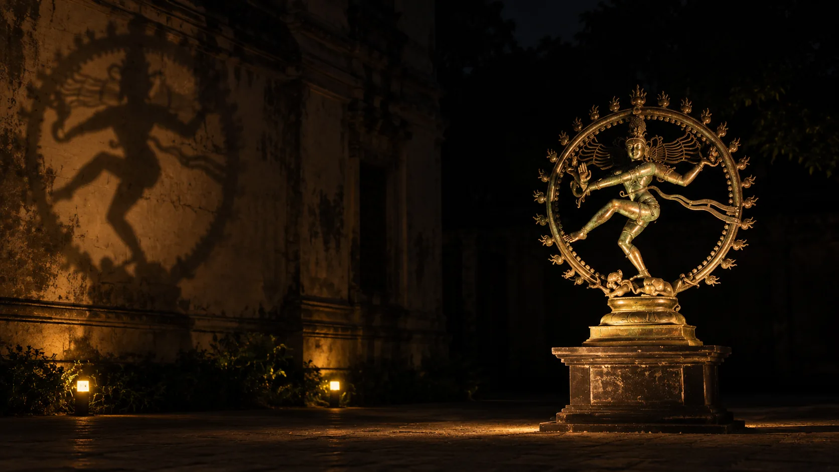 A bronze Nataraja lit at night beside a temple wall, its dancing shadow thrown large across the stone